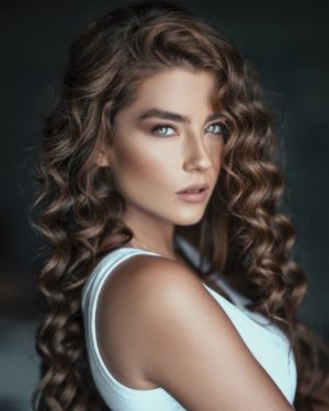 Hier zu sehen ist eine Frau mit gelockten Haaren und helleren Strähnen in braunem Haar | Trend Haarfarben 2020 - Hair&Style Altbach