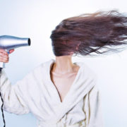 Hier zu sehen ist eine Frau im Bademantel, die ihre Haare stylt und dabei ins Gesicht föhnt | Tipps gegen fettige Haare - Hair&Style Altbach